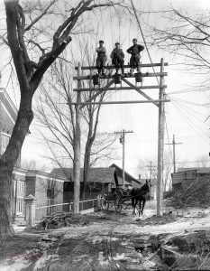 3 Men standing on top of an electric pole